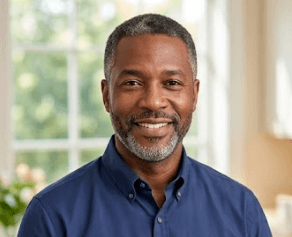 Smiling middle-aged Black man with salt-and-pepper hair and beard in a blue button-down shirt.