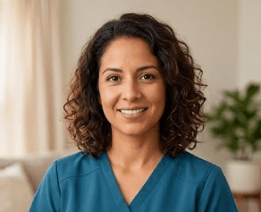 Smiling woman with curly brown hair wearing teal scrubs in a bright indoor setting.