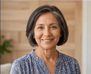 Smiling mature woman with short grey hair wearing a blue floral blouse in a home.