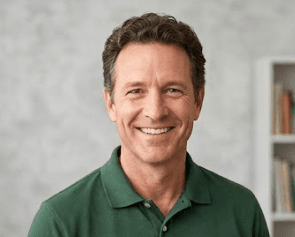 Middle-aged man with wavy brown hair smiling warmly in a green polo shirt.